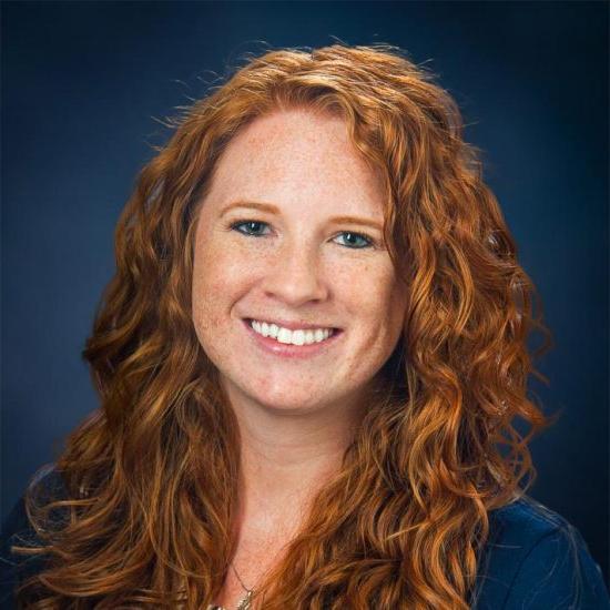 A smiling woman with curly red hair against a dark blue background.